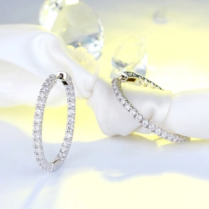 Macro detail of silver hoop earrings featuring pavé set round zircon on white silk