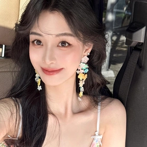 Détail de boucles d'oreilles fleurs colorées avec de longs pompons portées par un mannequin