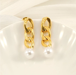 Detail of gold Cuban chain earrings with round pearls on a white shell plate