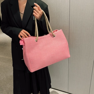 Detail of pink woven tote bag showing beige rope handles and metal eyelets on fabric