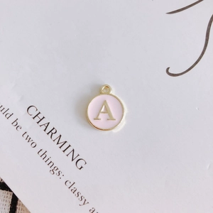 Macro detail of round pink enamel letter A pendant with gold-plated metal border