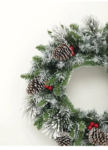 Close-up of artificial pine needles with snow effect, pine cones, and red berries decor