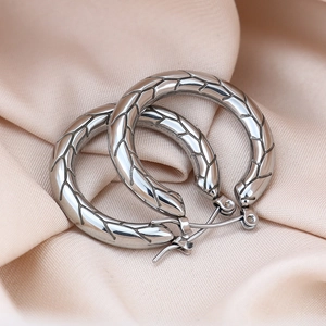 Macro view of silver stainless steel hoop earrings with textured leaf pattern on silk