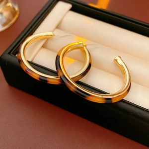 Detail of C-shaped tortoiseshell resin hoop earrings with elegant gold metallic trim