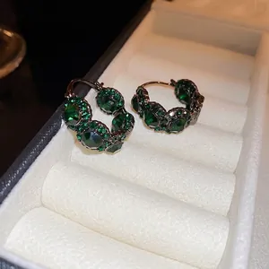 Retro gun-black hoop earrings with emerald green gemstones on white jewelry cushion