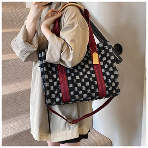 Close-up of large canvas tote bag featuring black and white plaid with red fringe straps