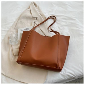 Minimalist caramel brown tote bag with slim shoulder straps on white bedding background