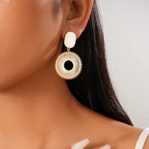 Détail de boucles d'oreilles rondes dorées avec motif en fil beige sur mannequin