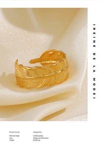 Detailed macro view of a gold-plated feather ring on soft white silk fabric background