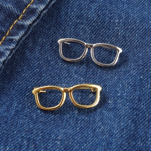 Close-up of gold and silver eyeglass-shaped brooches pinned on blue denim fabric