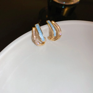 Macro shot of gold C-shaped earrings with light blue enamel and sparkling zircon accents