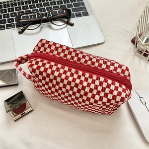 Close-up of red and white checkered velvet makeup bag with zipper and handle on a desk