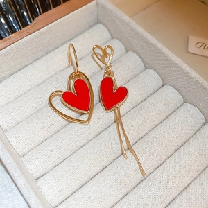 Macro detail of asymmetric hollow heart earrings with red enamel and golden tassels