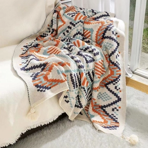 Bohemian knit throw blanket with navajo geometric patterns and fringe on white sofa