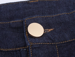 Dettaglio ravvicinato di jeans in denim blu scuro con bottoni dorati e cuciture arancioni
