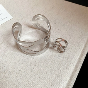 Detail of silver hollow geometric bracelet and ring set on minimalist textured fabric