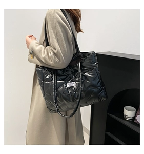 Side view of a large black padded tote bag with a fashion label on a beige coat model