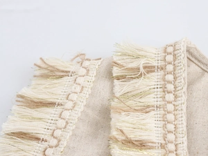 Détail des franges tissées sur une robe bohème beige avec des fils dorés