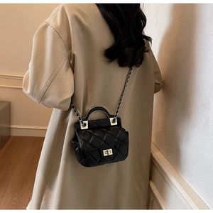 Detail of black quilted chain bag with metallic handle on beige trench coat