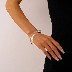 Close-up of a wide wavy acrylic transparent bracelet on a model's wrist with black clothing