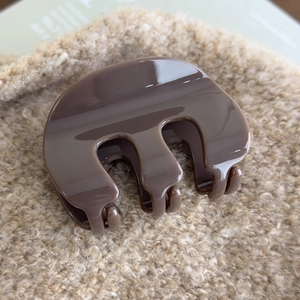 Close-up of a glossy brown M-shaped hair claw clip on soft beige plush background