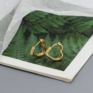 Artistic close-up of sweet heart-shaped gold hoop earrings placed on a green fern leaf book