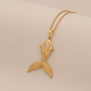 Detail of a golden fish pendant with a white oval opal stone on a thin O-chain necklace