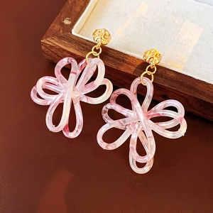 Dettaglio macro di orecchini a fiore in resina rosa con perni dorati su vassoio di legno