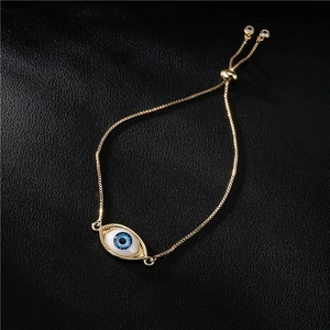 Adjustable golden evil eye bracelet with blue center stone on a black leather background