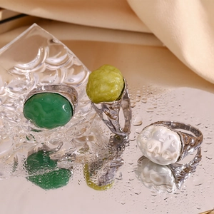 Detail of silver rings with irregular green and white stones on a reflective water surface