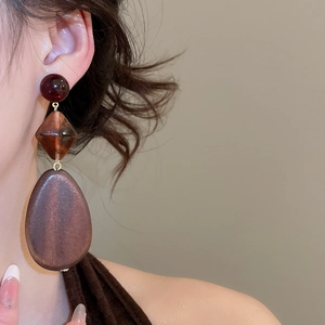 Close-up of three-tier geometric wood drop earrings worn by a model in warm light