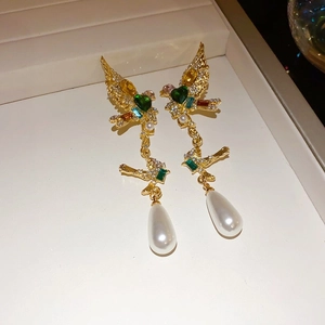 Close-up of golden bird earrings with colorful crystals and hanging white drop pearls