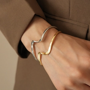Minimalist irregular twisted gold and silver bangles worn on a model with a blazer