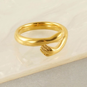 Detail view of gold hug ring showing minimalist hand-shaped design on marble background