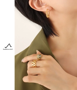 Close-up of gold-plated stainless steel twisted hoop earrings and natural stone rings