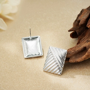 Detailed view of silver rectangular stud earrings with diagonal textured ridges on wood