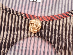 Détail d'un bouton nœud doré sur une robe en résille à rayures et liseré orange vif