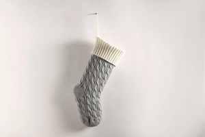 Close-up of grey and cream cable knit Christmas stocking hanging on a neutral wall