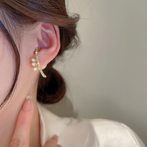 Close-up of curved gold ear cuff with shimmering crystals and three white pearls
