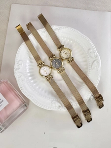 Elegant gold quartz watches with Milanese mesh bands displayed on a decorative tray