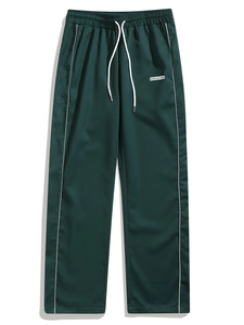 Detail of dark green woven joggers featuring white side stripes and a drawstring waist