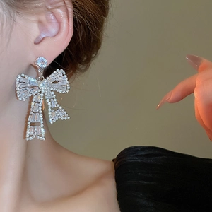 Close-up of bow earrings with trapezoid zircon stones worn by a model for a luxury look