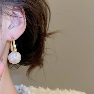 Close-up of elegant round pearl earrings with golden U-shaped pendants on model