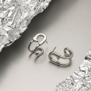 Detail of silver stainless steel safety pin earrings on a modern industrial metal background
