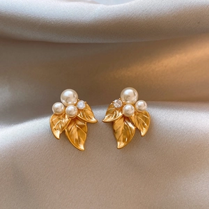 Macro shot of gold leaf earrings with white pearls on elegant champagne silk fabric