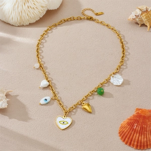 Goldene Halskette mit Herz-Anhänger, bösem Blick und Muschel auf sandigem Strand