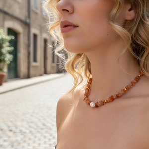 Detail of vintage necklace with orange gemstones and a central white pearl on a model