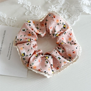 Detailed close-up of pink floral scrunchie with white lace edges on a white background
