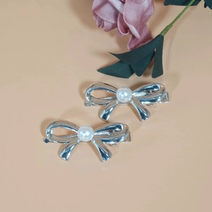 Pair of silver metal bow hair clips with pearls on a soft beige background décor