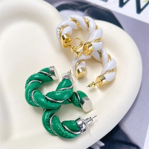 Detail of twisted leather and polished metal C-shaped hoop earrings on a ceramic tray